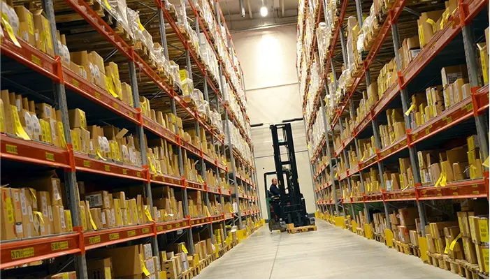 A forklift operator driving down a fully stocked warehouse aisle.