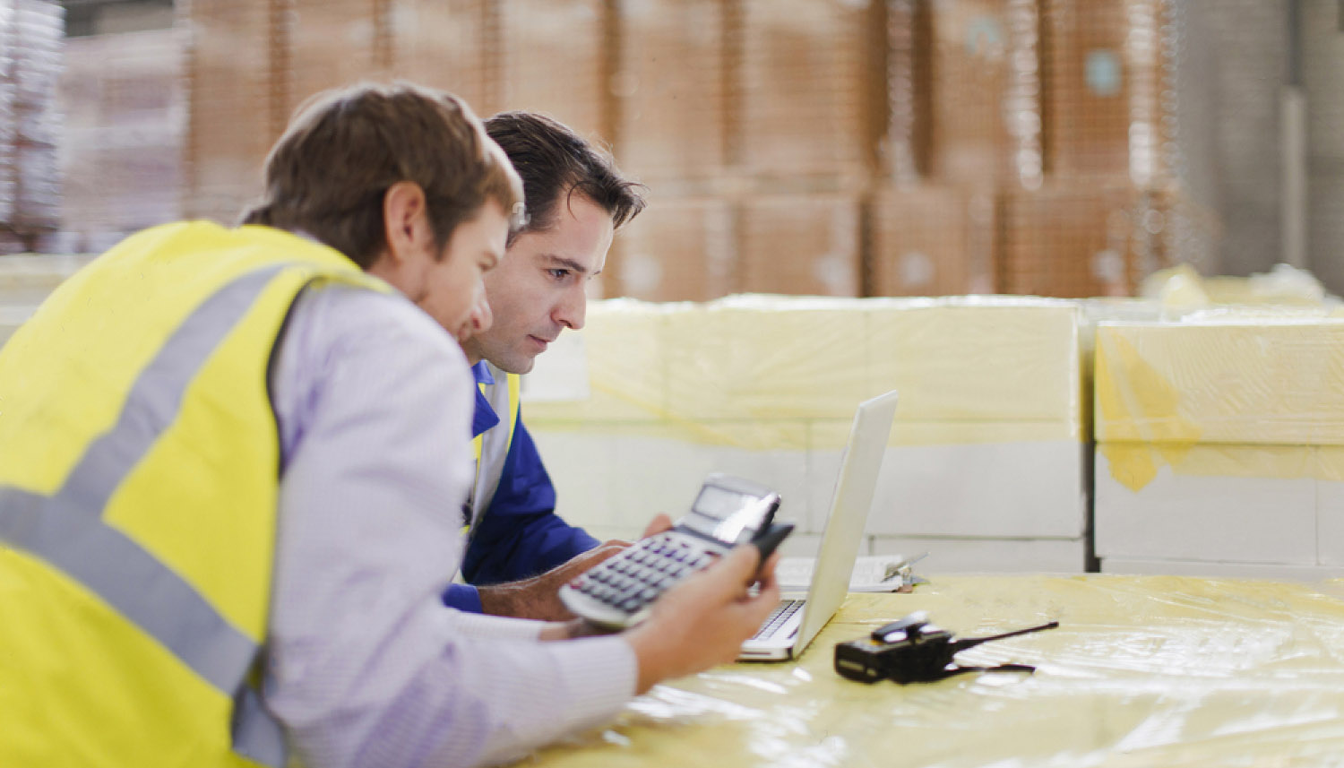 Two men comparing shipping costs at a computer inside a warehouse.